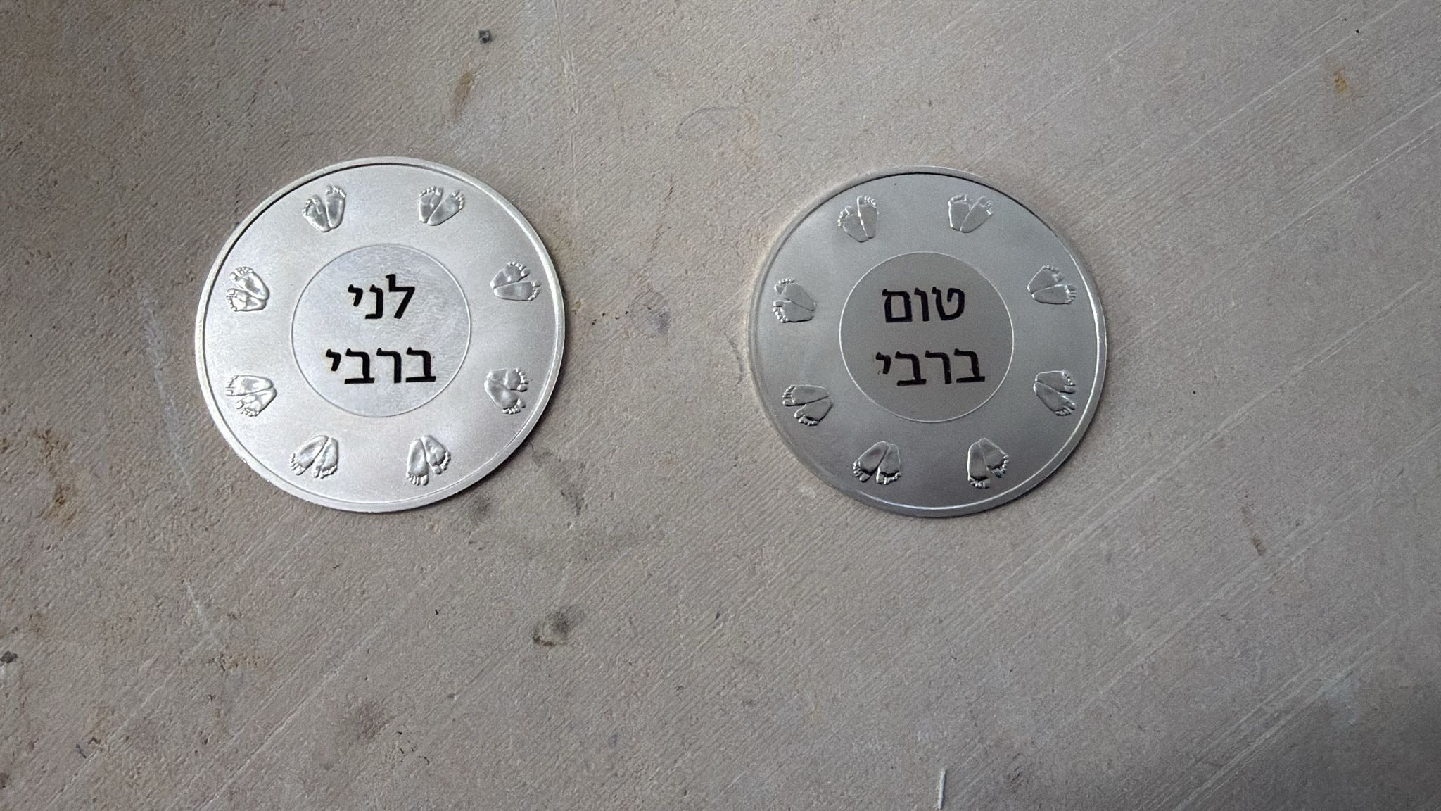 חריטה על זוג מטבעות כסף בעיצוב כפות רגליים של תינוק עם השמות לני ברבי וטום ברבי