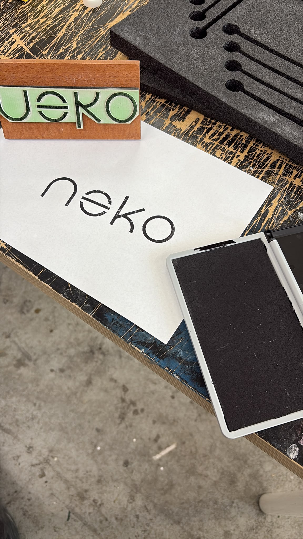 חריטה על חותמת עץ עם גלופה ללוגו neko לצד הטבעה על נייר