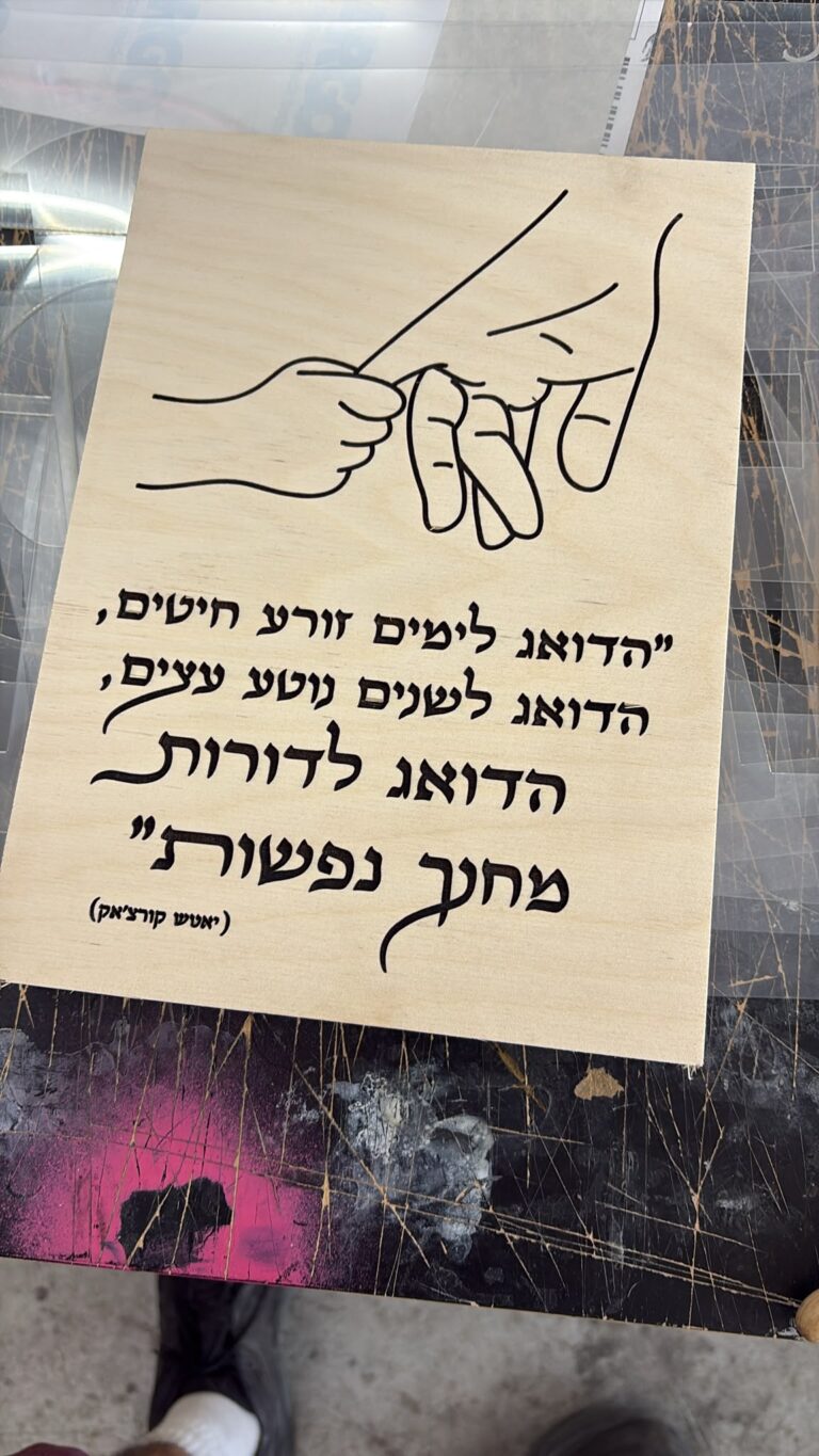 חריטה על לוח עץ עם ציור קווי של שתי ידיים וציטוט יאנוש קורצ'אק הדואג לדורות מחנך נפשות