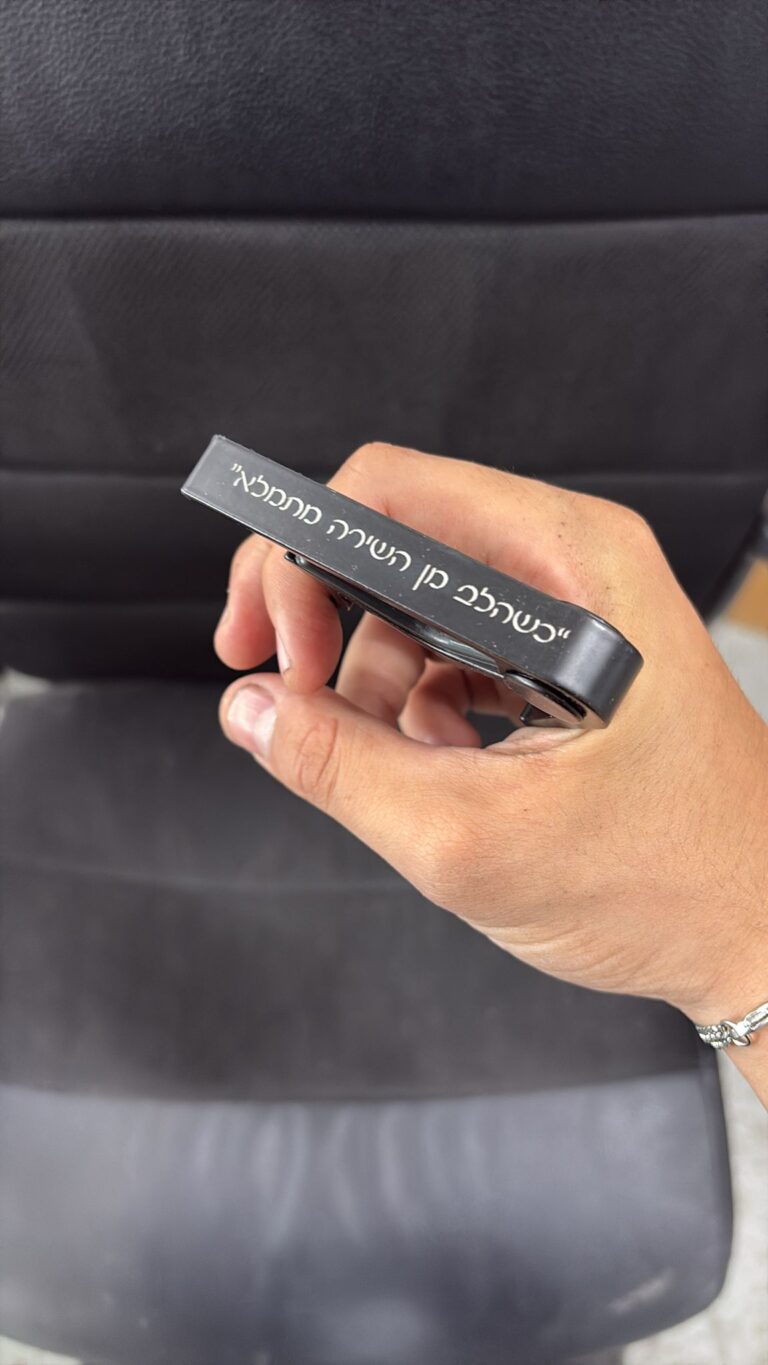 חריטה על קאפו לגיטרה מתכת שחור עם הכיתוב כשהלב מן השירה מתמלא
