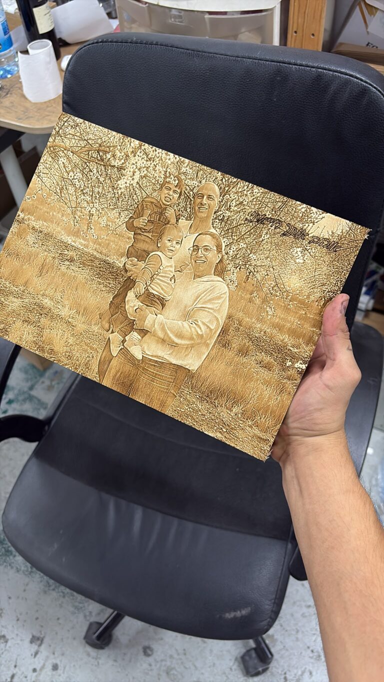 חריטה של תמונת משפחה עם שני ילדים בשדה פורח על לוח עץ עם הקדשה אוהבים אותך המון